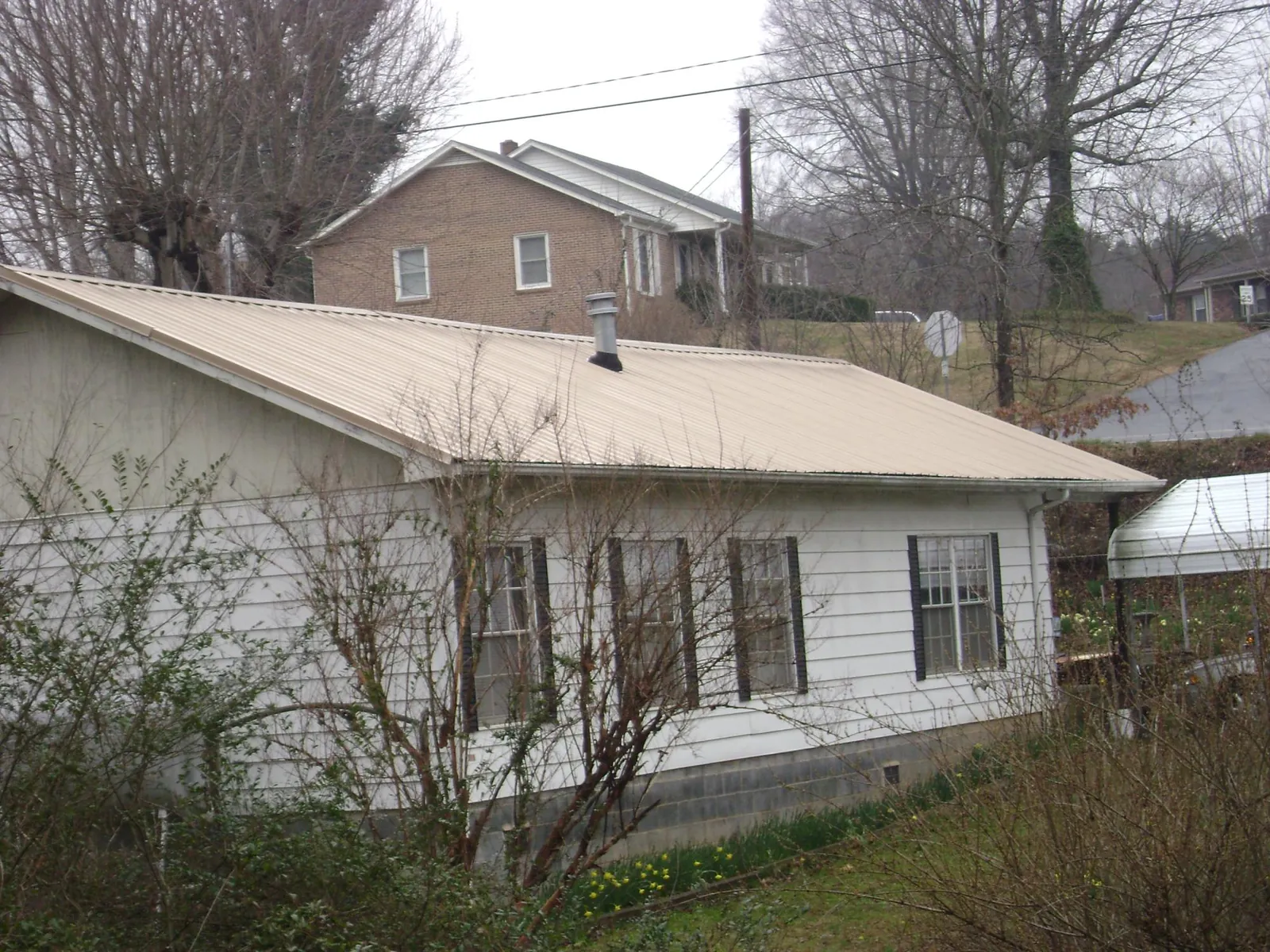 Tan metal roof on a white sided house set into a hillside — Commercial Roofing by Roofing Brothers in Linden